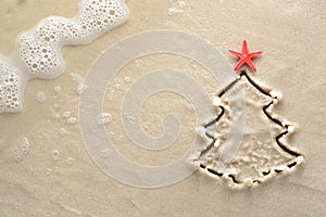 Holiday background - Christmas tree with starfish drawn on a sandy beach