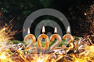 Holiday background Happy New Year 2023. Digits of year 2023 made by burning gold candles on red festive sparkling