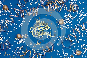 Holiday background with Merry Christmas wording, golden confetti, balls and ribbons on classic blue