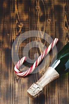 Holiday Bottle of champagne and candy canes over wooden background. Christmas and New Year celebration. Bottle with Sparkling Wine