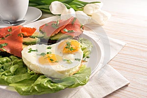 Holiday breakfast with love, fried eggs in heart shape, sandwiches with avocado and smoked salmon on lettuce, white tulips on a