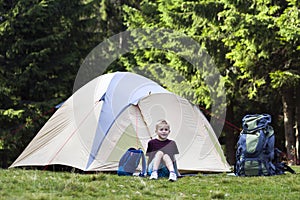 Holiday camping. Young boy sitting in front of a tent near backpacks taking rest after hiking in the forest shows something in th