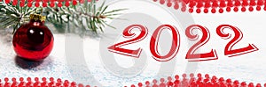 Holiday card New Year 2022 banner. A red Christmas ball and a snow-covered tree branch on a snowy white background.