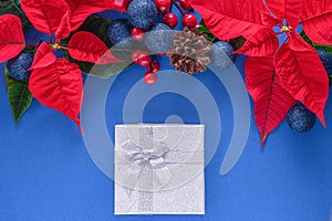 Holiday card - red flower poinsettia, fir cone, Christmas decorations on blue background. Flat lay, top view