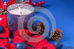 Holiday card - red flower poinsettia, scented candle in blue glass holder on blue background. Christmas decorations