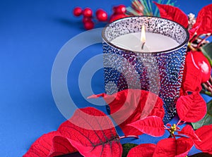 Holiday card - red flower poinsettia, scented candle in blue glass holder on blue background. Christmas decorations