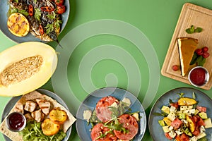 Holiday celebration table setting with food. Flat-lay of sweet cheesecake, fruit salad, meat dishes. Copy space banner.