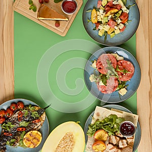 Holiday celebration table setting with food. Flat-lay of sweet cheesecake, fruit salad, meat dishes. Copy space banner.