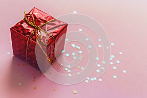 Holiday christmas greeting card. Present red gift box with golden bow ribbon on pink background