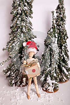 Holiday Christmas wintery scene with wooden jointed doll standing holding gift wearing Santa Claus hat