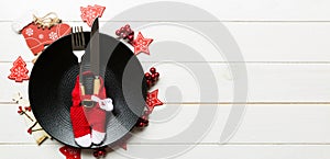 Holiday composition of plate and flatware decorated with Santa clothes on wooden background. Banner Top view of Christmas