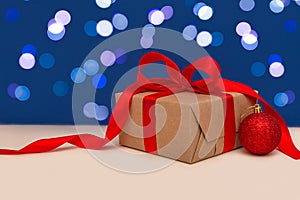 Holiday concept. Christmas gift box with red bow and christmas red ball on blue bokeh background. Holiday greeting card. Copy