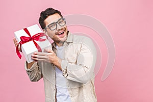 Holiday concept. Portrait of a young man opening gift box isolated over pink background