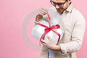 Holiday concept. Portrait of a young man opening gift box isolated over pink background