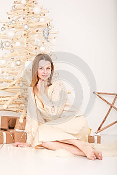 holiday concept. Young beautiful woman in light elegant evening dress sitting on floor by the Christmas tree and gift