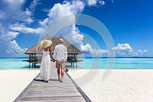 A holiday couple in summer clothing walks hugging over a pier at a tropical beach