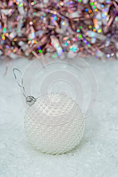 Christmas. White ball nacre pearls on a snow and beautiful blurred colorful background of glittering bokeh with glowing lights.