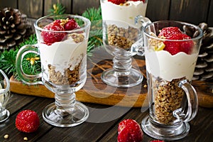 Holiday dessert with cream, muesli, fresh strawberry, sauce, cheesecake and yogurt on rustic wooden background close up