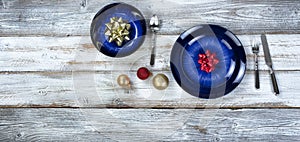 Holiday dinner table setting of an empty main dark blue dish and bowl with Christmas or New Years decorations plus cutlery on