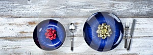 Holiday dinner table setting of a main dark blue dish and bowl with Christmas or New Years bow decorations plus cutlery on rustic