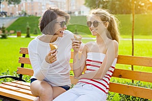 Holiday with the family. Happy young mother and cute daughter teenager in city park eating ice cream, talking and laughing