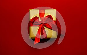 Holiday gift. Box in a gold gift wrapping with a red bow, on a red background. Merry Christmas, Happy New Year and