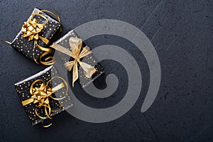 Holiday gift box or present with ribbon, golden confetti and gold baubles on black background. Magic christmas greeting card. Chri
