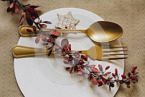 Holiday Gold place setting, white plate of concrete, with fork and golden spoon. Christmas or tanksgiving dinner. From above