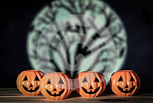 Holiday halloween with four toy pumpkins on wooden table, horizontal moon with dead tree background and voodoo tone.