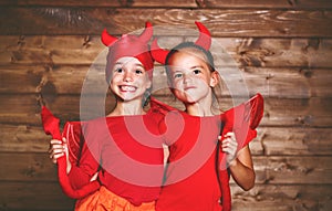 holiday halloween. funny funny sisters twins children in carnival costumes devil on wooden