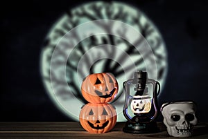 Holiday halloween with two toy pumpkins, toy lantern pumpkin, toy skull on wooden table, moon with dead tree background.