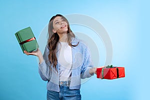 Excited young beautiful girl holding gift boxes isolated on blue studio background. Concept of emotions, Merry Christmas