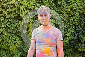 Holiday, holi and people concept - Man with open mouth and with green powder on his shirt and face over bush background