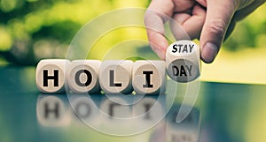 Holiday at home concept. Hand turns a cube and changes the word `holiday` to `holistay`