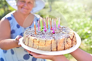 Holiday homemade cake in close-up hands. Smiling grandmother is holding a birthday homemade cake. Family celebrating grandmother`