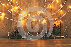 Holiday image with Christmas golden garland lights and pine cones over wooden background