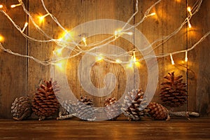 Holiday image with Christmas golden garland lights and pine cones over wooden background