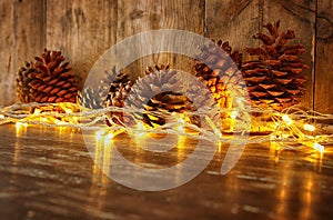 Holiday image with Christmas golden garland lights and pine cones over wooden background