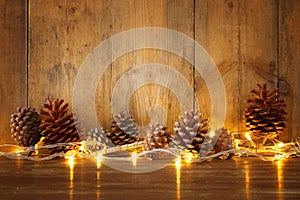 Holiday image with Christmas golden garland lights and pine cones over wooden background