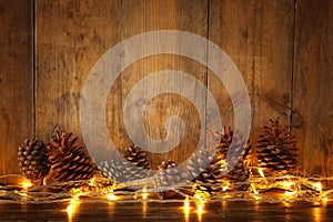 Holiday image with Christmas golden garland lights and pine cones over wooden background