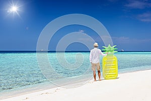 Holiday man standing a tropical paradise beach and holding a yellow floaty