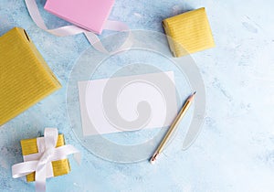 Holiday mockup: top fiew flat lay gold and pastel pink gift boxes with white ribbon, empty card and pencil on blue background. Gre