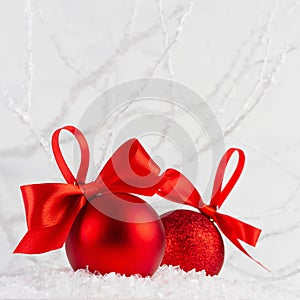 Holiday New Year background with two shine glitter glossy red balls with bright scarlet ribbon in white decorative snow, frosty.