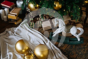 Holiday, New Year& x27;s gift boxes and wooden horse toy under decorated Christmas tree with golden baubles, garland in