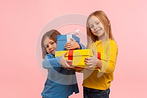 Holiday present for kids. Two happy little girls holding gifts together and smiling at camera, children embracing christmas