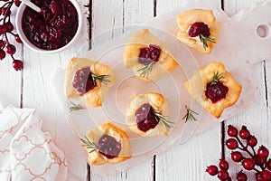 Holiday puff pastry appetizers with cranberries and baked brie, above view serving platter against white wood photo