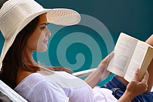 Holiday, reading and woman at pool with book, hat and relax with happy summer travel on hotel patio. Vacation, deck