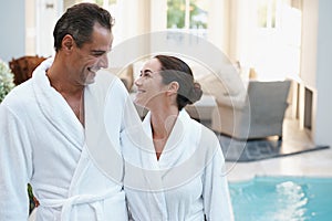 Holiday, robe and couple at hotel pool with smile, embrace and relax together at wellness spa getaway. Hospitality