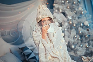 Holiday is ruined! Young beautiful woman in knitted hat and scarf rolled in plaid having flu and blowing her nose at handkerchief