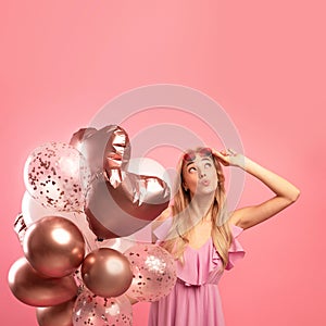 Holiday sale concept. Cute blonde woman holding bunch of balloons, pursing her lips and looking upwards at copy space